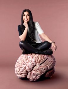 Dr. Samantha Yammine sitting on a model of a brain.